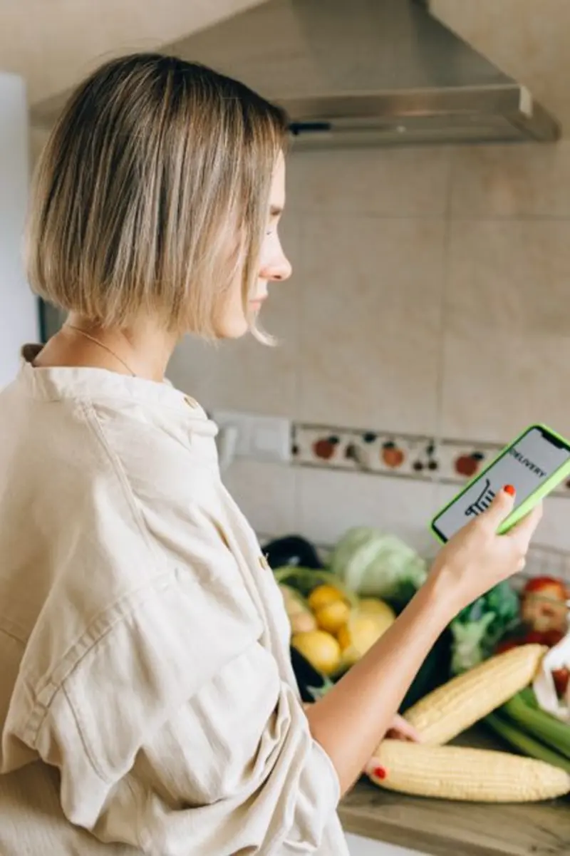 Frau in der Küche spricht ihre Mahlzeit ins Handy